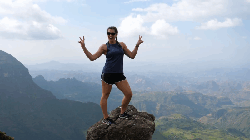 A woman stands on a rock at the edge of a cliff in the Simien Mountains