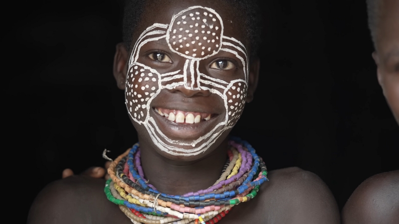 A Karo child from Ethiopia smiles with white face paint and colorful beaded necklaces during a traditional ceremony