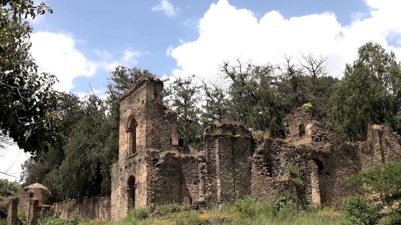 Ruins of the Kuskuam Complex in Gondar, Ethiopia, with stone walls and arched structures surrounded by trees and grass