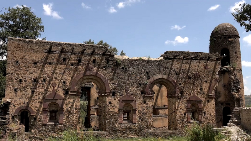 Qusquam Mariam Church in Gondar, Ethiopia, with arched stone walls and a round tower under a clear blue sky
