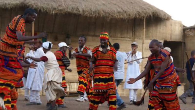 Wolayta men dance in colorful traditional clothing during a cultural celebration in front of a thatched building